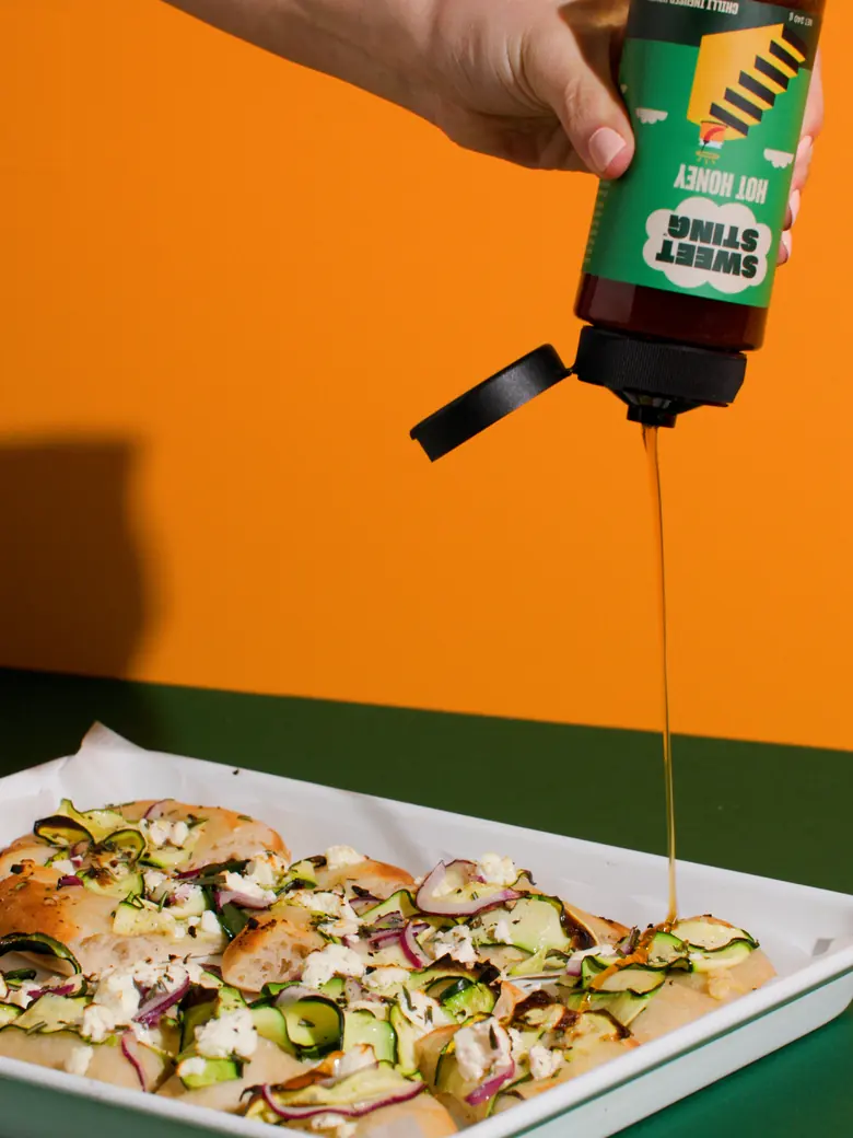 Sweet Sting hot honey drizzled over flatbread on an orange background